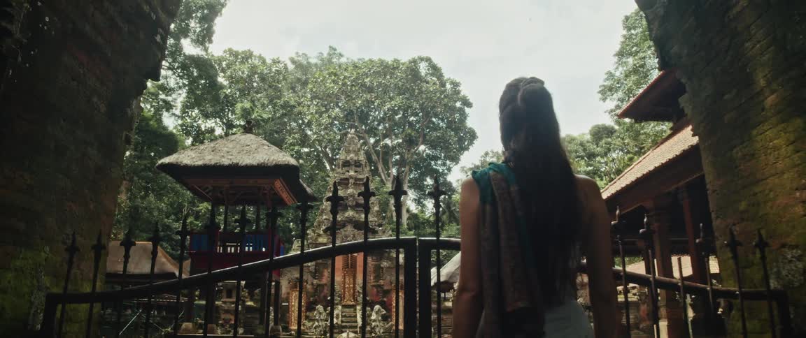 A young woman traveler stands at the ancient gate of a serene Balinese temple, surrounded by a lush tropical jungle