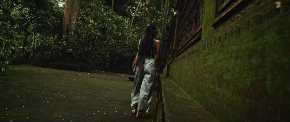 A woman gracefully explores an ancient, moss-covered temple deep within a lush, green jungle