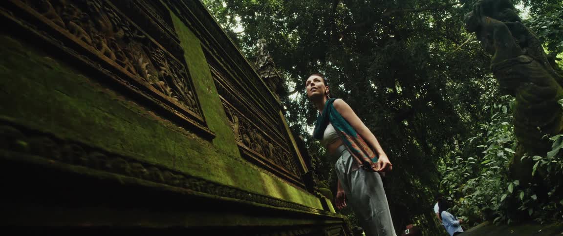 A curious woman marvels at the majestic, moss-laden stone walls of a forgotten temple hidden in the forest