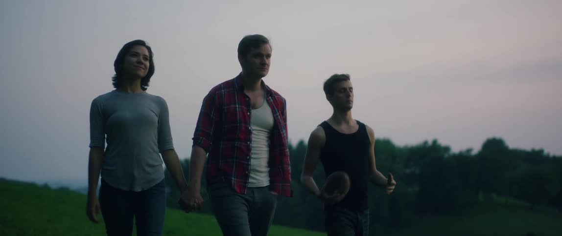 A man and woman walk holding hands while another man plays with a football