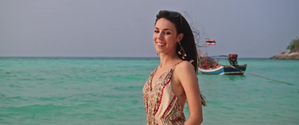 A happy woman in a summer dress smiles and enjoys the breeze on a beautiful tropical beach in Thailand in slow motion