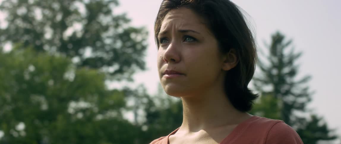 Worried looking woman stands outside among trees