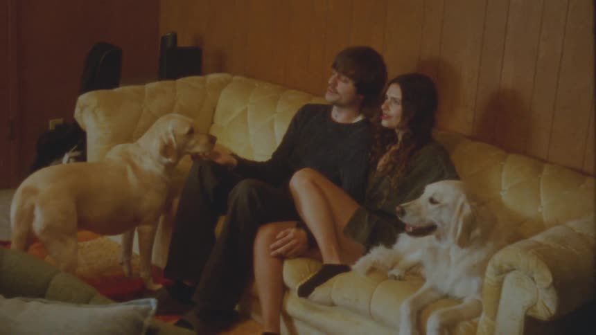 A happy couple enjoys a cozy moment at home, petting and talking to their two beautiful dogs on the couch