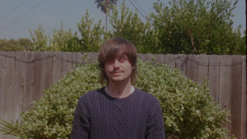 A vintage film-style portrait of a young man smiling and closing his eyes in a sunny backyard