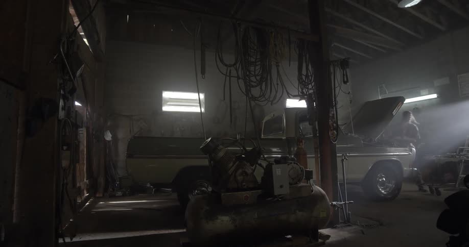 A person works on a pickup truck engine in a garage