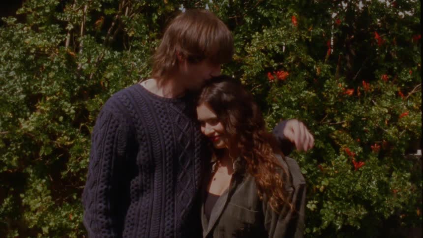 A young couple shares a romantic kiss and a tender embrace in a sunlit garden in this vintage-style footage