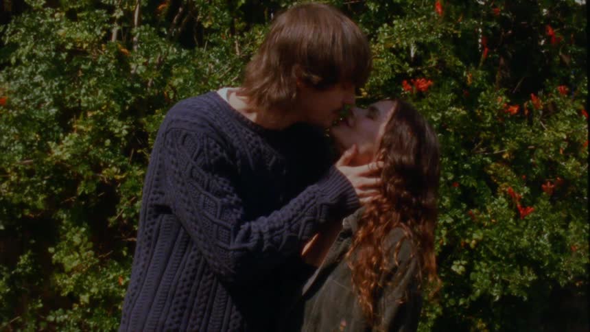 Vintage-style footage of a young couple sharing a passionate kiss in a sunny garden