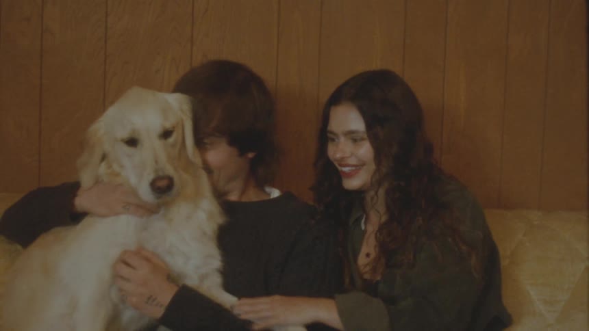 A happy young couple affectionately pets their beautiful golden retriever while sitting together on a couch at home