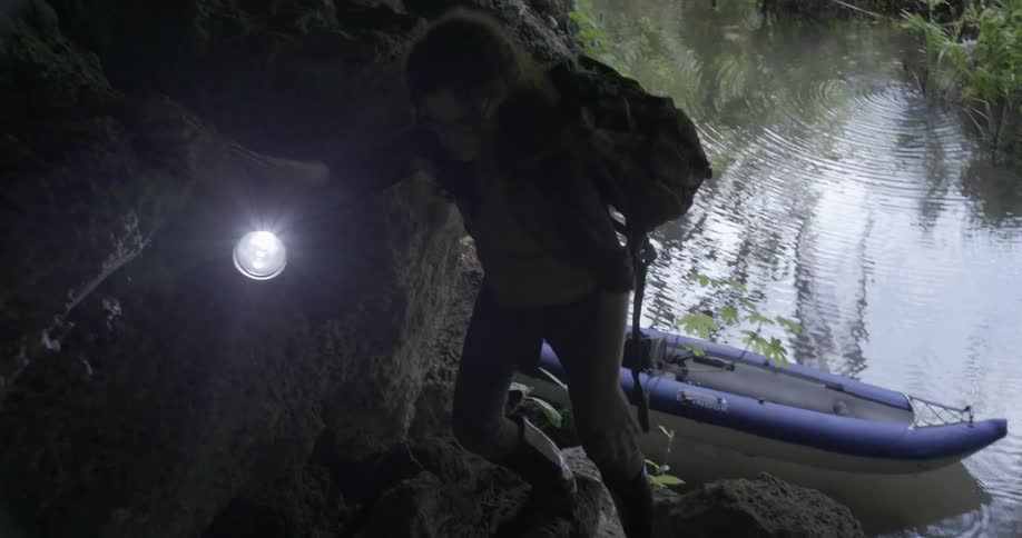 Woman wearing backpack exploring cave with flashlight
