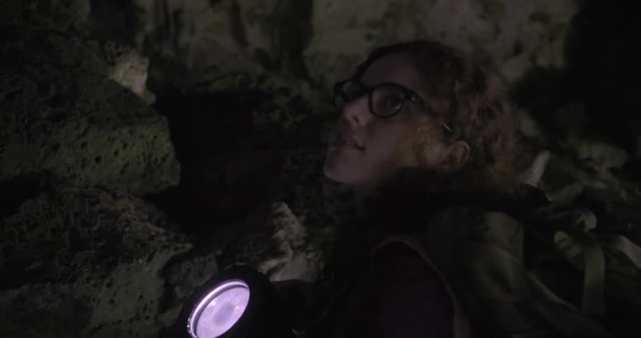 A woman carrying a flashlight climbs up a rocky hill