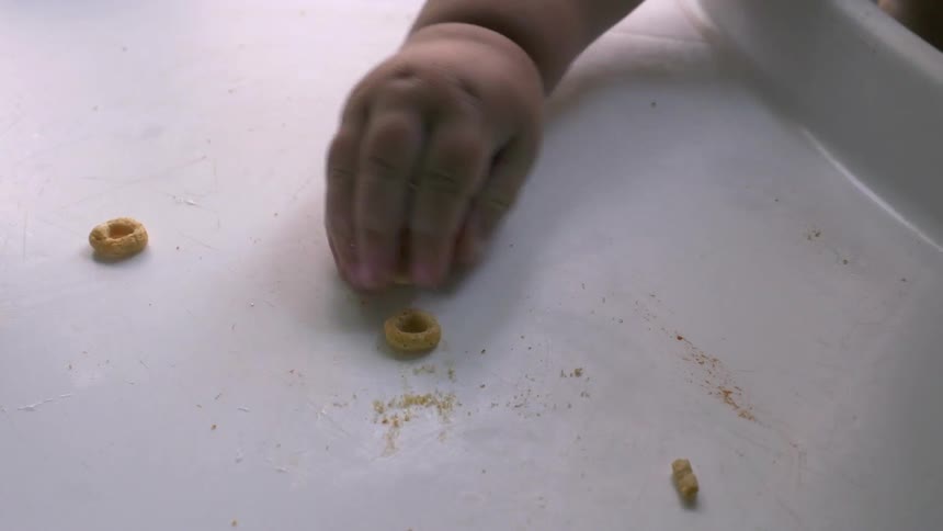 A baby grabs cereal off of the top of a high chair