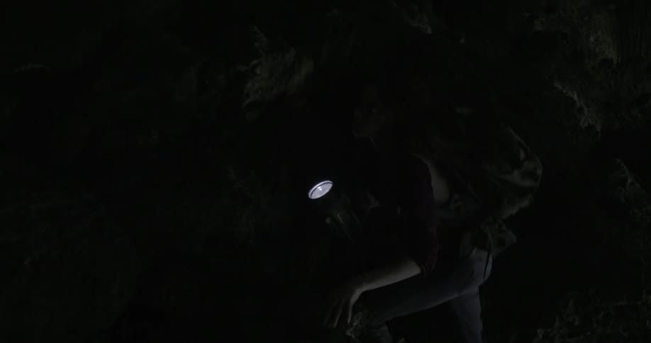 A woman carries a flashlight as she climbs through a dark cave