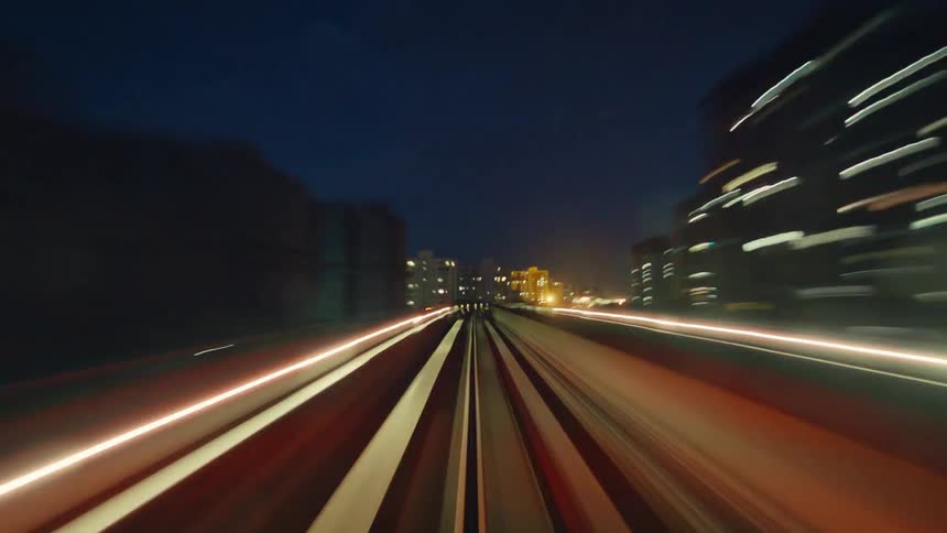 A high-speed point-of-view time-lapse from a monorail train as it races through a futuristic city at night, creating mesmerizing light trails