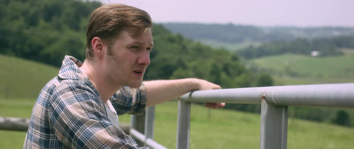 A man leans against a fence on a farm