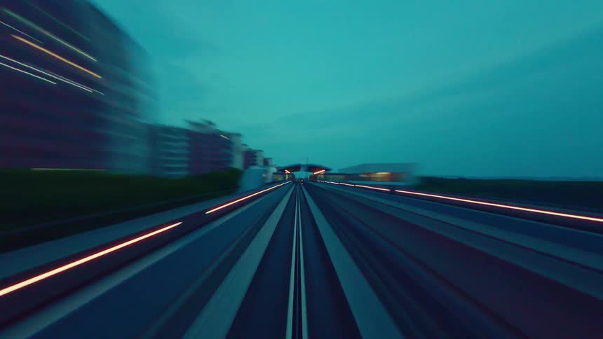 A futuristic point-of-view timelapse captures a high-speed monorail journey at dusk, creating vibrant streaks of light through the city