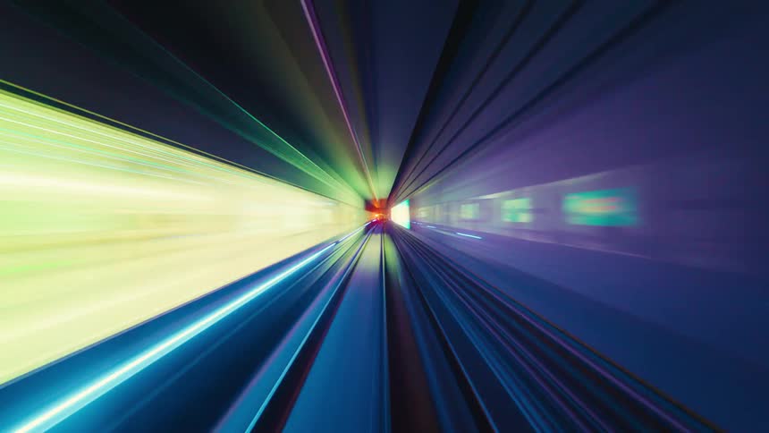 An abstract and futuristic point-of-view time-lapse of a high-speed train ride through a colorfully lit underground tunnel