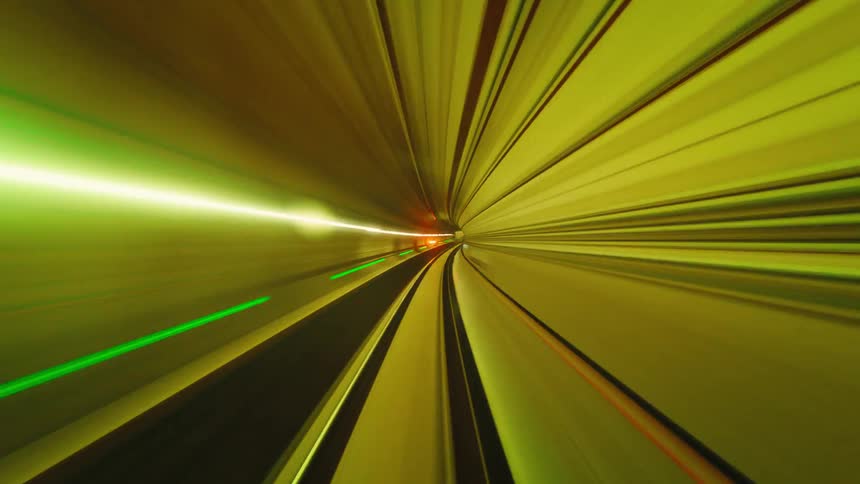 An abstract and futuristic point-of-view time-lapse of a high-speed train ride through a colorfully lit underground tunnel