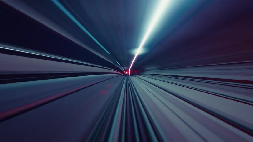 An abstract, futuristic time-lapse from a high-speed train blurs colorful lights into streaks while racing through a dark subway tunnel