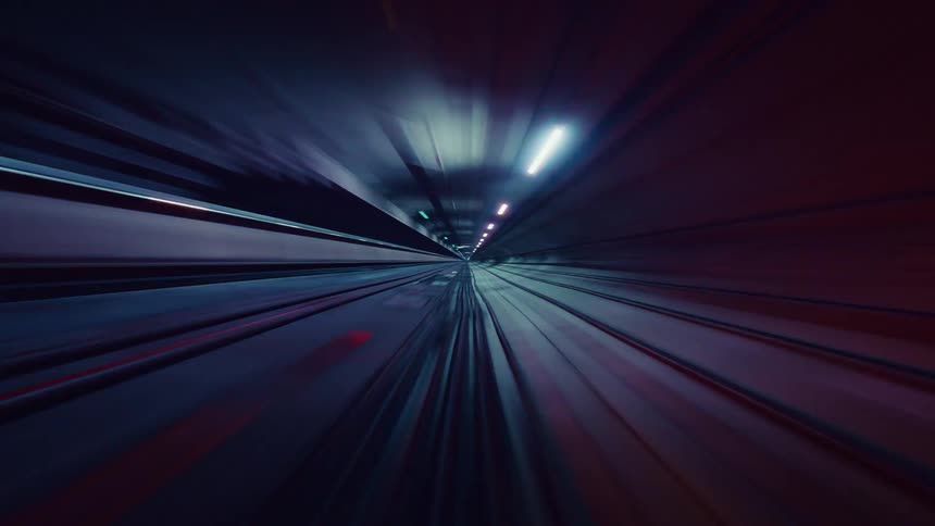 An abstract, futuristic time-lapse from a high-speed train blurs colorful lights into streaks while racing through a dark subway tunnel