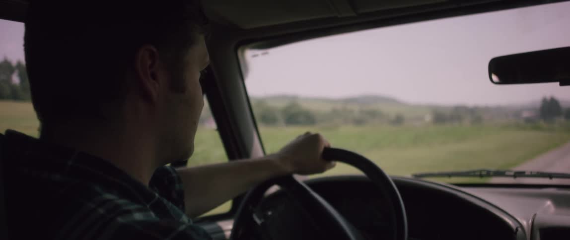 A man is driving a car near a large field