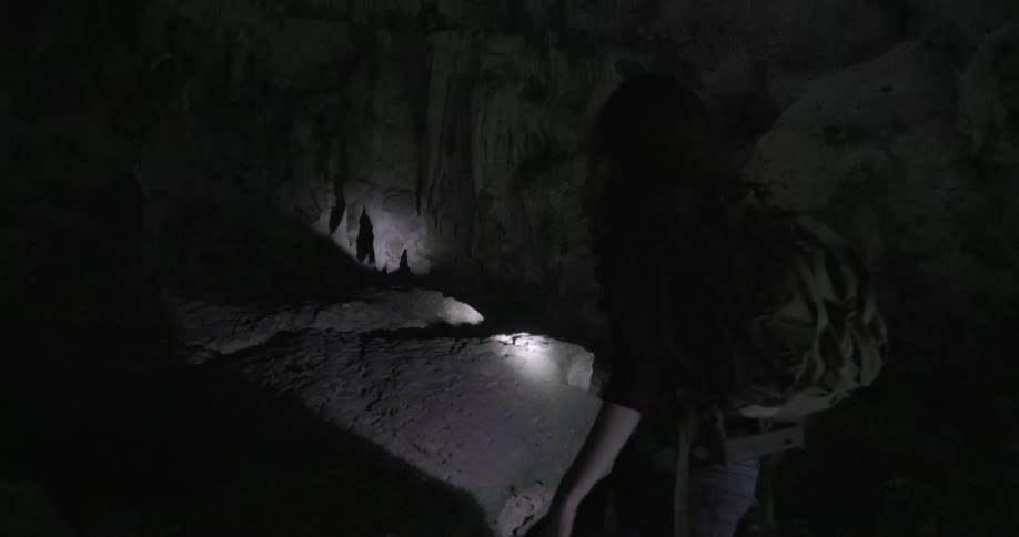 A woman shines a flashlight in a dark cave