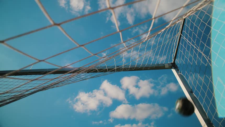 Low angle shot of a soccer ball scoring a goal as it flies into the net against a clear blue sky