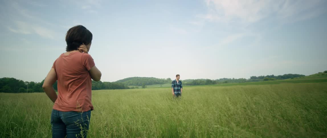 A woman stands looking at a man in the grass