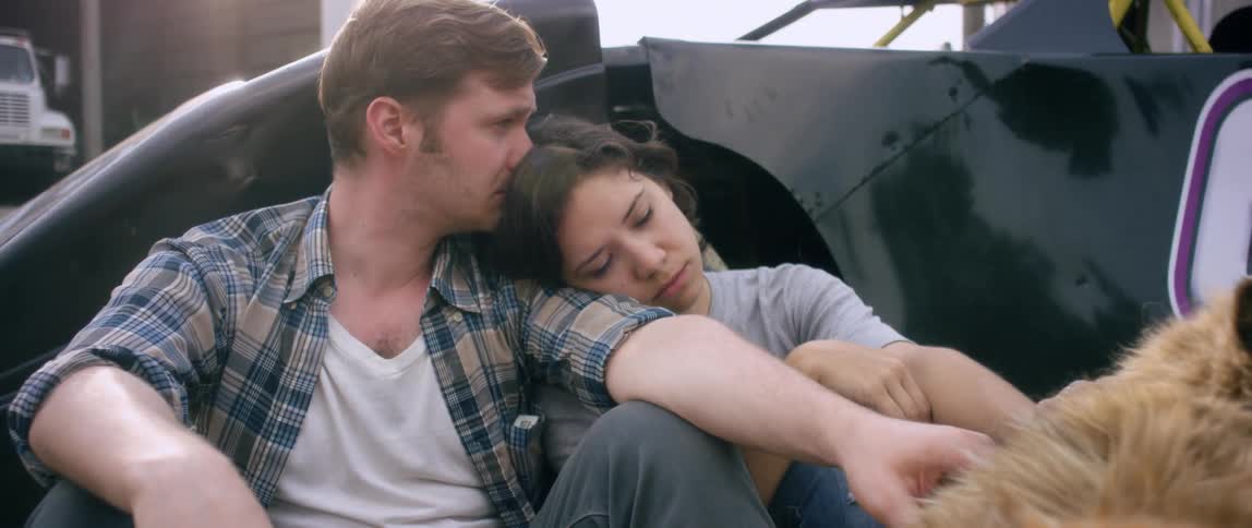 A man and woman rest on each others shoulders as the man smokes a cigarette