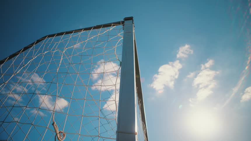 A soccer goal net sways gently in the breeze against a bright blue sky on a sunny day