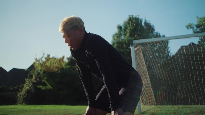 A young male athlete in black athletic wear stops to catch his breath on a sunny soccer field