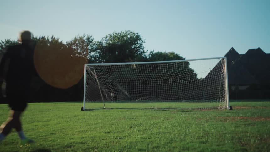 Slow motion tracking shot of a soccer player kicking the ball and scoring a goal on a sunny green field