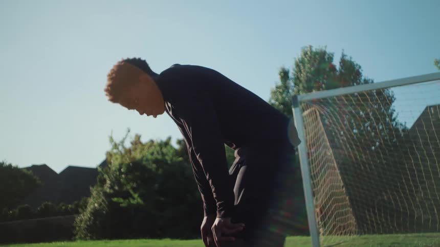 A young Black man in athletic gear catches his breath during a soccer workout before running again in slow motion