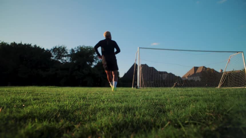 Slow-motion low-angle shot of a soccer player kicking a ball and scoring a goal on a grassy field