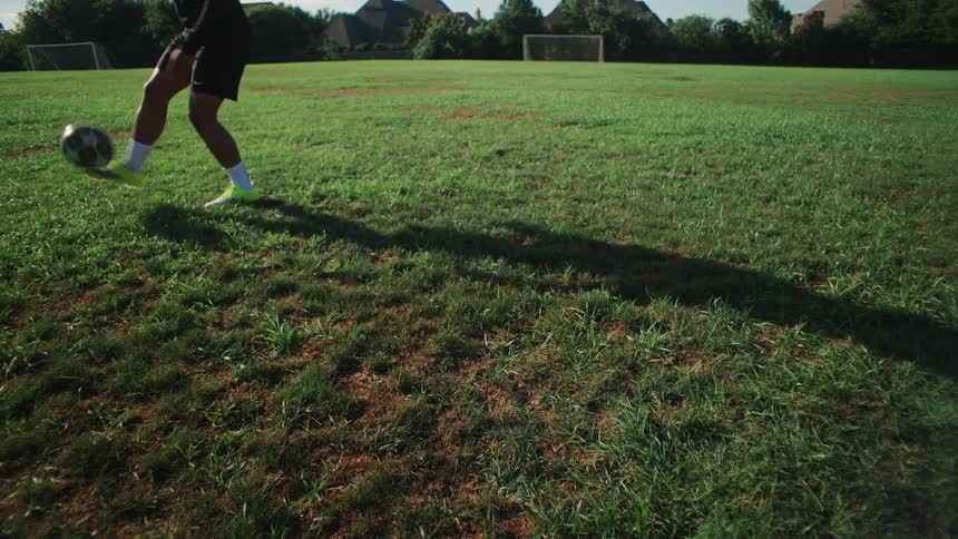 A close up of a soccer player's feet in slow motion juggling a soccer ball on a grassy field on a sunny day