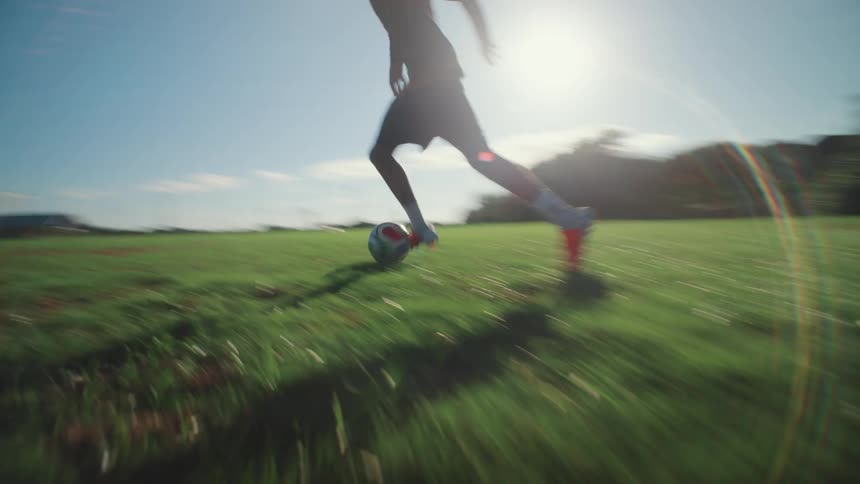 A soccer player's feet dribble a ball across a sunny green field in a fast-paced, low-angle shot