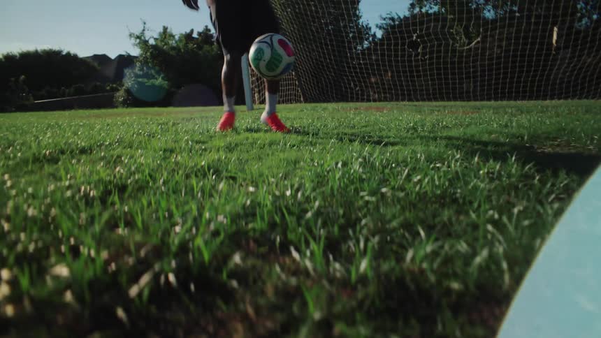 A soccer ball falls from the blue sky and is skillfully controlled by a player who dribbles across a sun-drenched green field