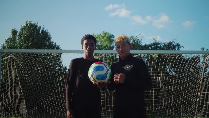 Two determined young multicultural soccer players stand together holding a ball in front of a goal