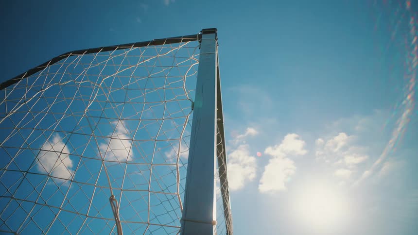 A soccer goal net flutters in the breeze on a sunny day with a clear blue sky