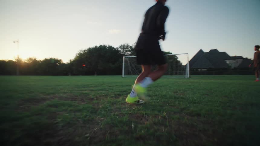 A young man scores a goal in slow motion on a grassy soccer field during a beautiful sunset