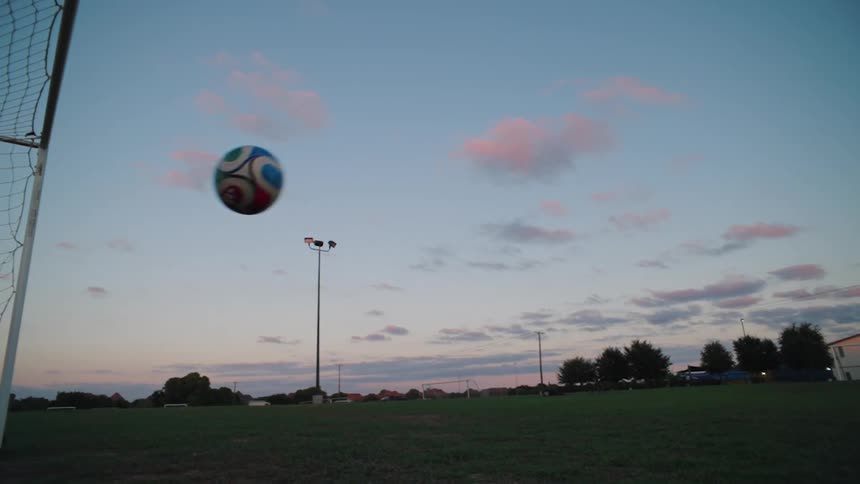 Slow motion shot of a soccer ball soaring into the upper corner of the goal net at dusk