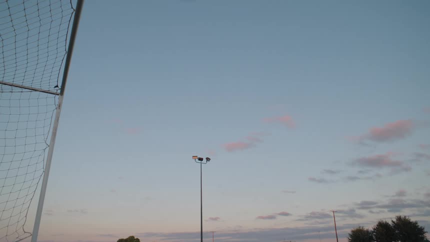 Slow motion shot of a soccer ball soaring into the top corner of the goal at dusk