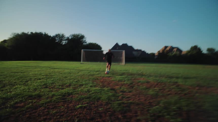 Fast-paced action shot follows a young soccer player skillfully dribbling a ball down a green field at golden hour