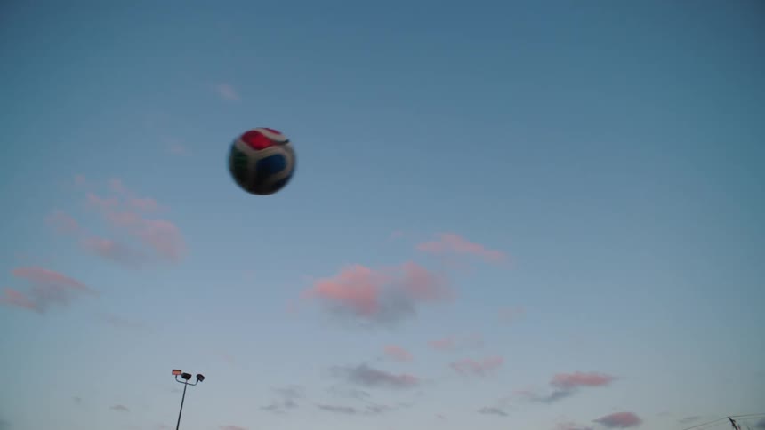 A soccer ball flies in slow motion through a dusky blue sky with pink clouds