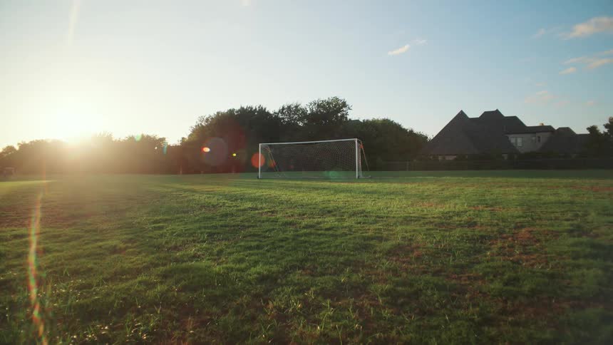 A serene, empty soccer field bathed in the golden light of the rising sun, with a prominent lens flare