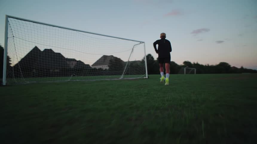 A soccer player skillfully dribbles the ball down a grassy field towards the goal at dusk