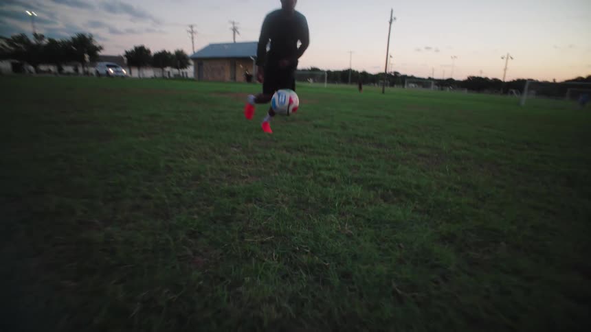 A talented young man skillfully juggles and dribbles a soccer ball down the field during a solo practice at dusk