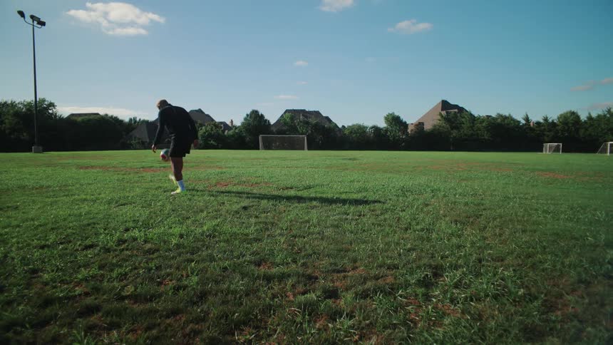 Wide shot of a male soccer player juggling a ball in slow motion on an empty green field