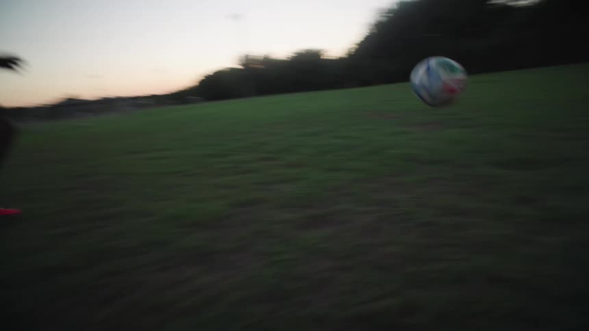 Slow motion POV shot following a soccer ball as a player dribbles down the field at dusk and takes a shot on goal
