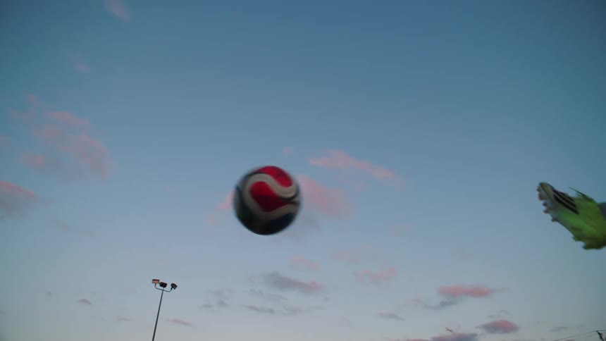 A soccer ball is kicked and soars through the air in slow motion against a beautiful dusky sky