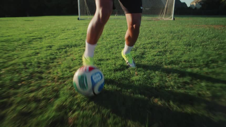 Dynamic close-up of a skilled young soccer player's feet dribbling a ball across a grassy field at sunset